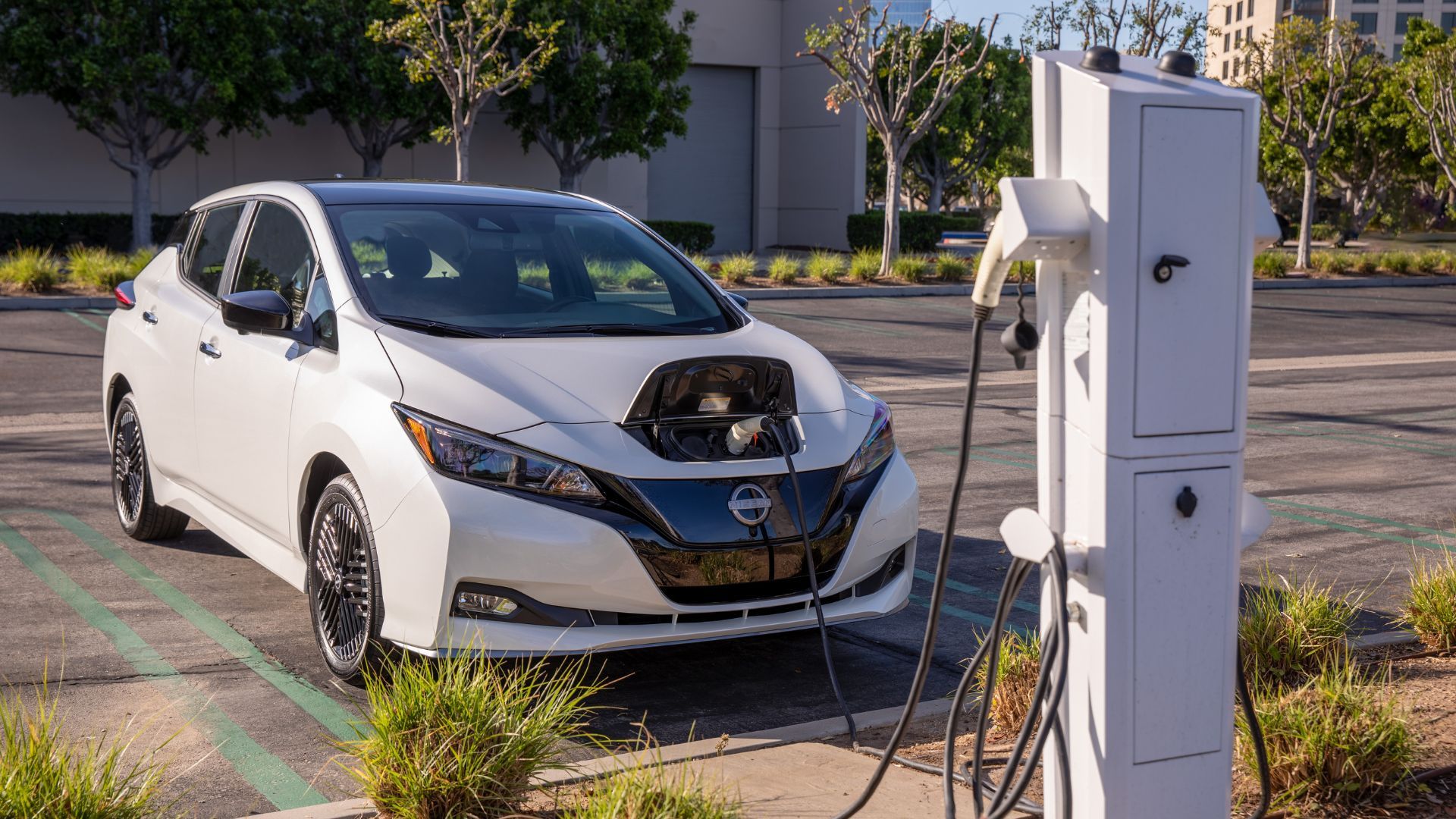 Static front 3/4 shot of a white 2023 Nissan Leaf plugged into a public charger.