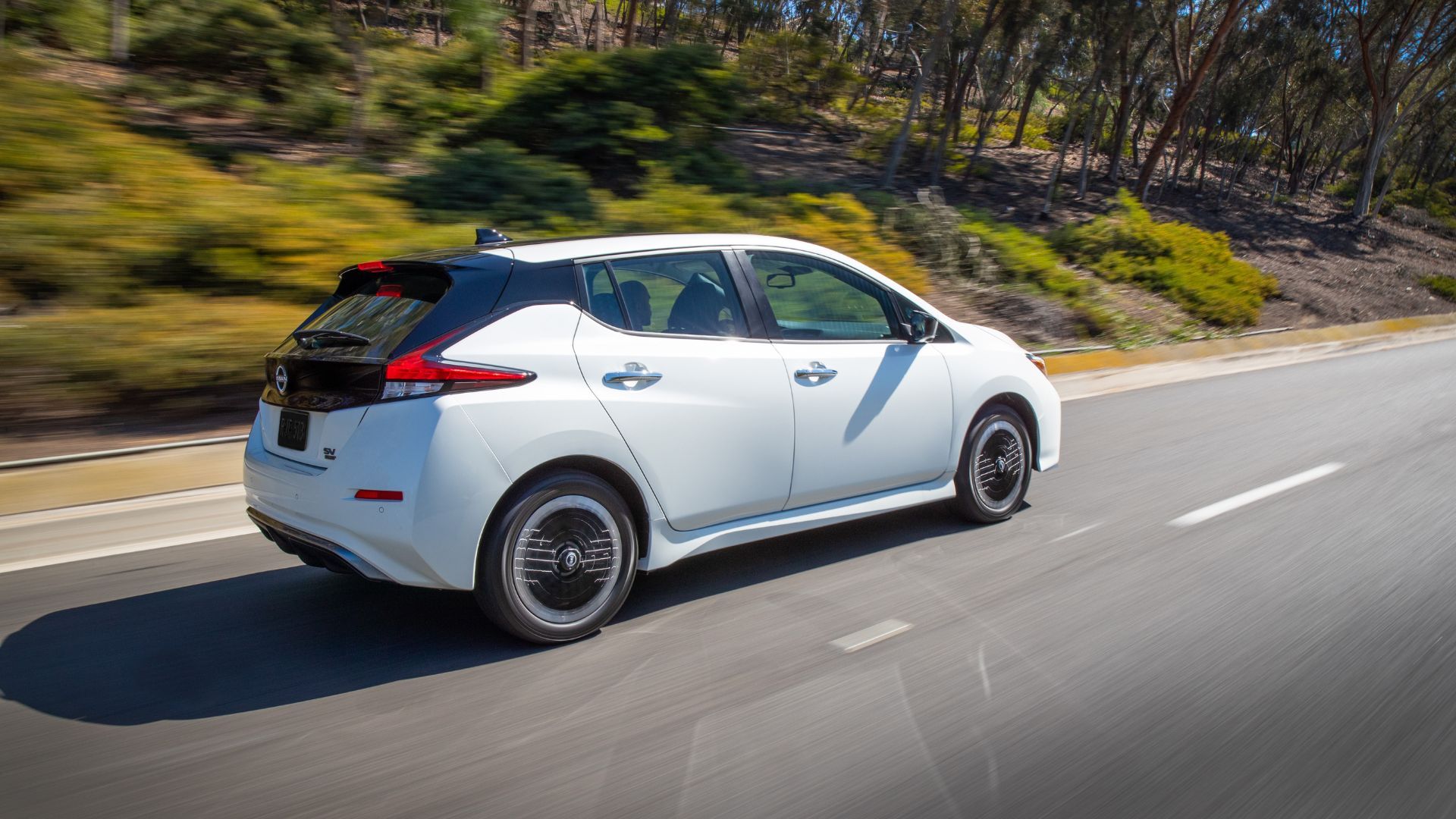 Dynamic rear 3/4 shot of a white 2023 Nissan Leaf driving on a country road.