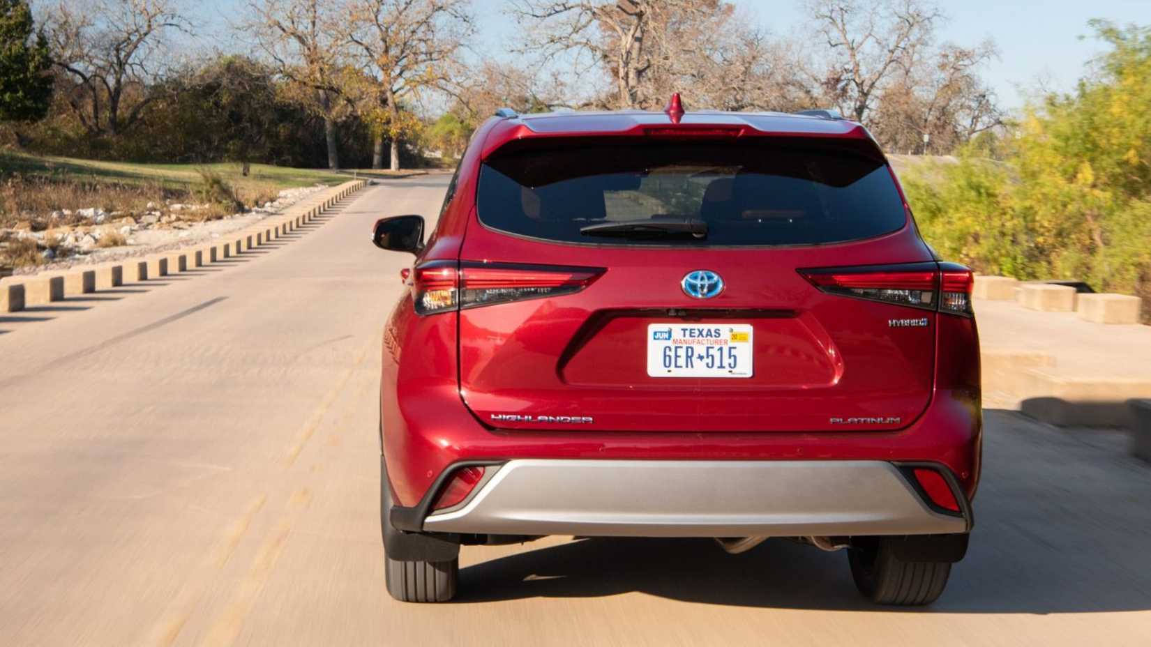 Dynamic rear-end shot of a red 2024 Toyota Highlander Hybrid driving on a country road.