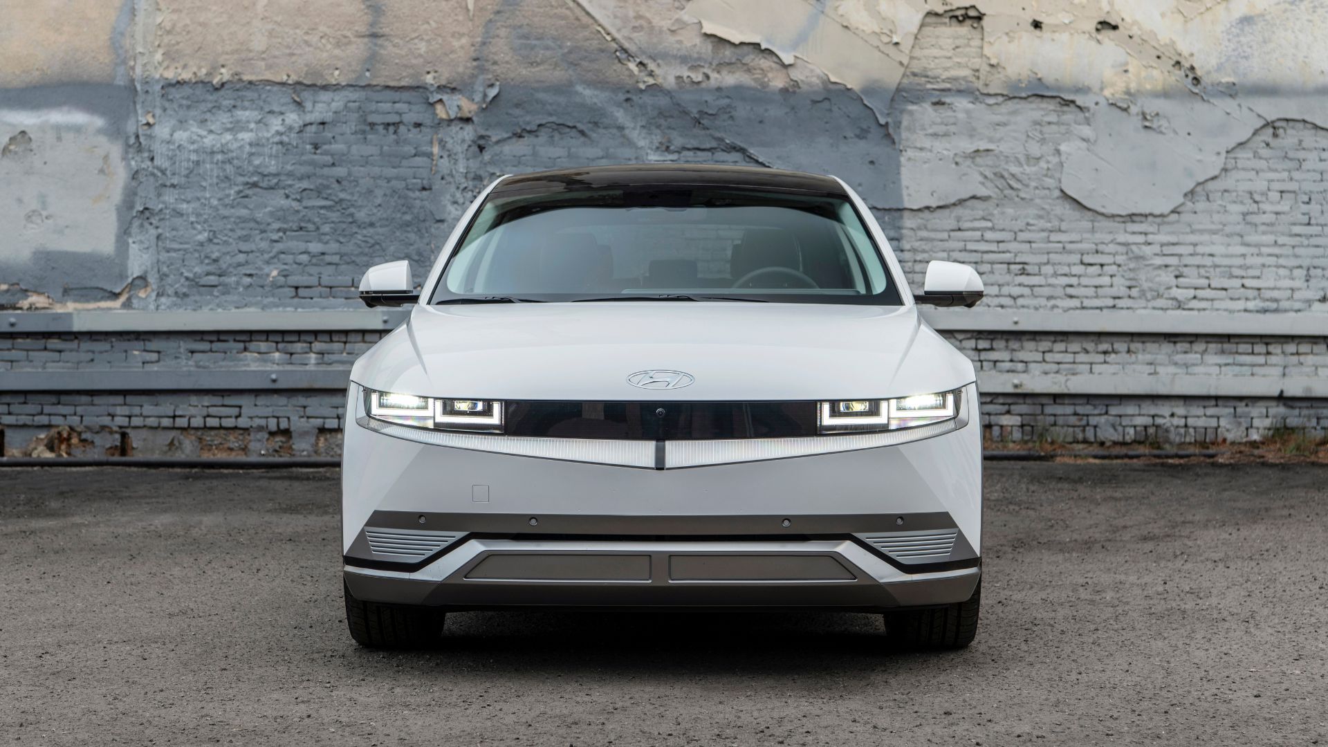 Статичный фронтальный снимок белого Hyundai Ioniq 5 2023 года на фоне кирпичной стены.
