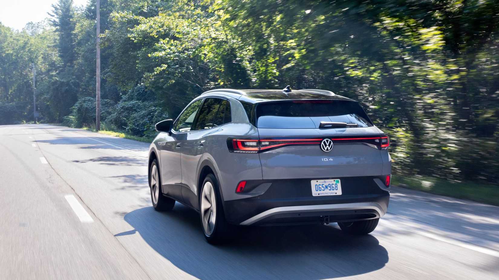 Dynamic rear 3/4 shot of a gray 2021 Volkswagen ID.4 driving on a country road lined by trees.