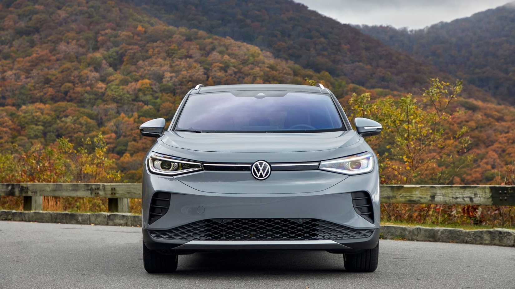 Static front-end shot of a gray 2021 Volkswagen ID.4 parked on gravel with hills in the background.