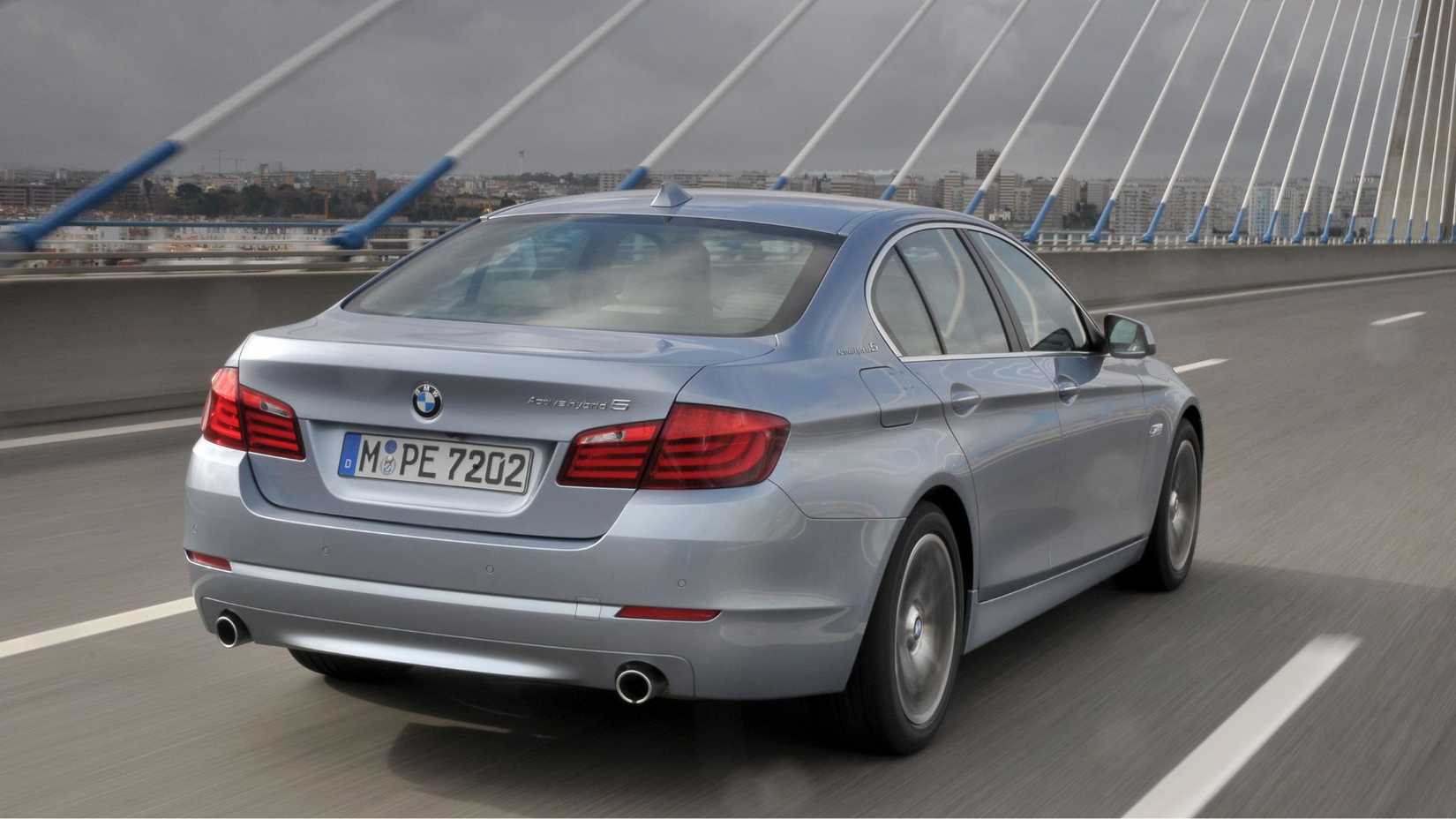 Dynamic rear 3/4 shot of a silver BMW ActiveHybrid 5 driving over a bridge.
