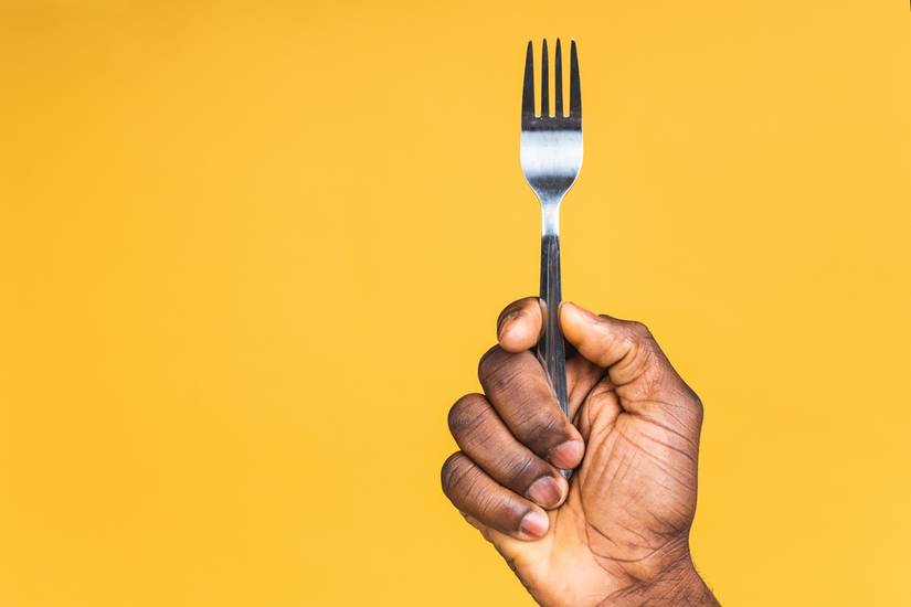 Close-up photo of african american male hand holding a fork isolated over yellow background.