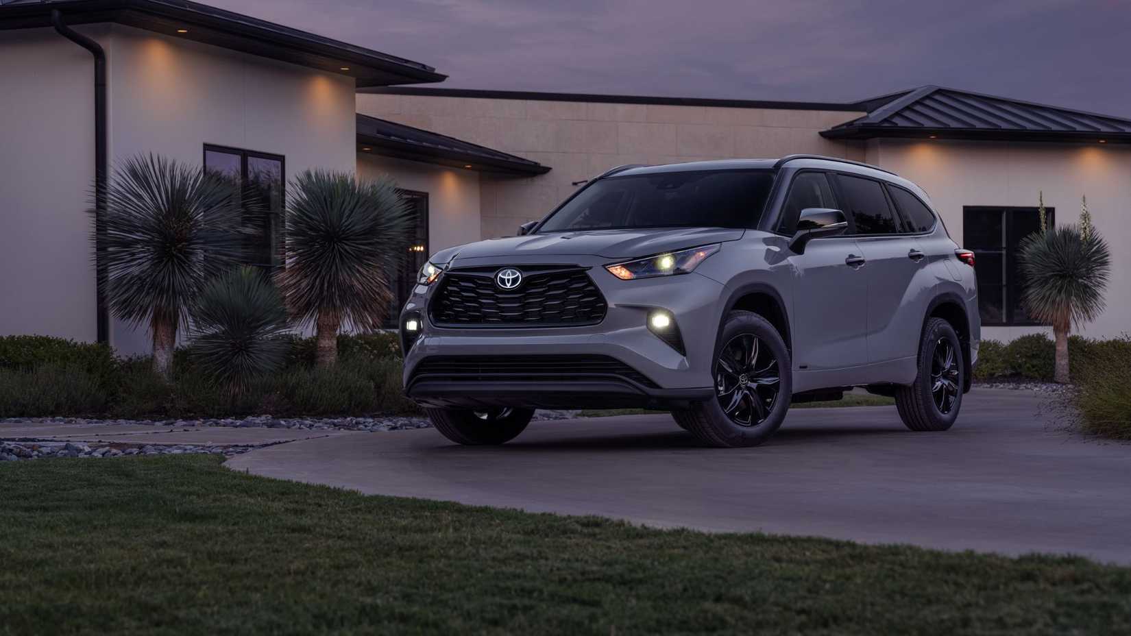 Static front 3/4 shot of a gray 2025 Toyota Highlander Hybrid parked on the driveway of a house.