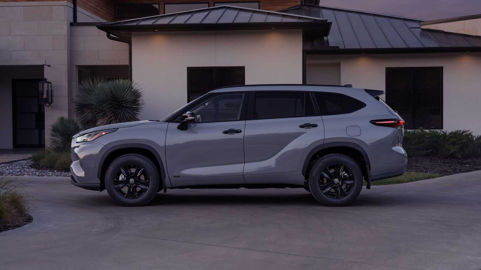 Static side profile shot of a gray 2025 Toyota Highlander Hybrid parked on the driveway of a house.