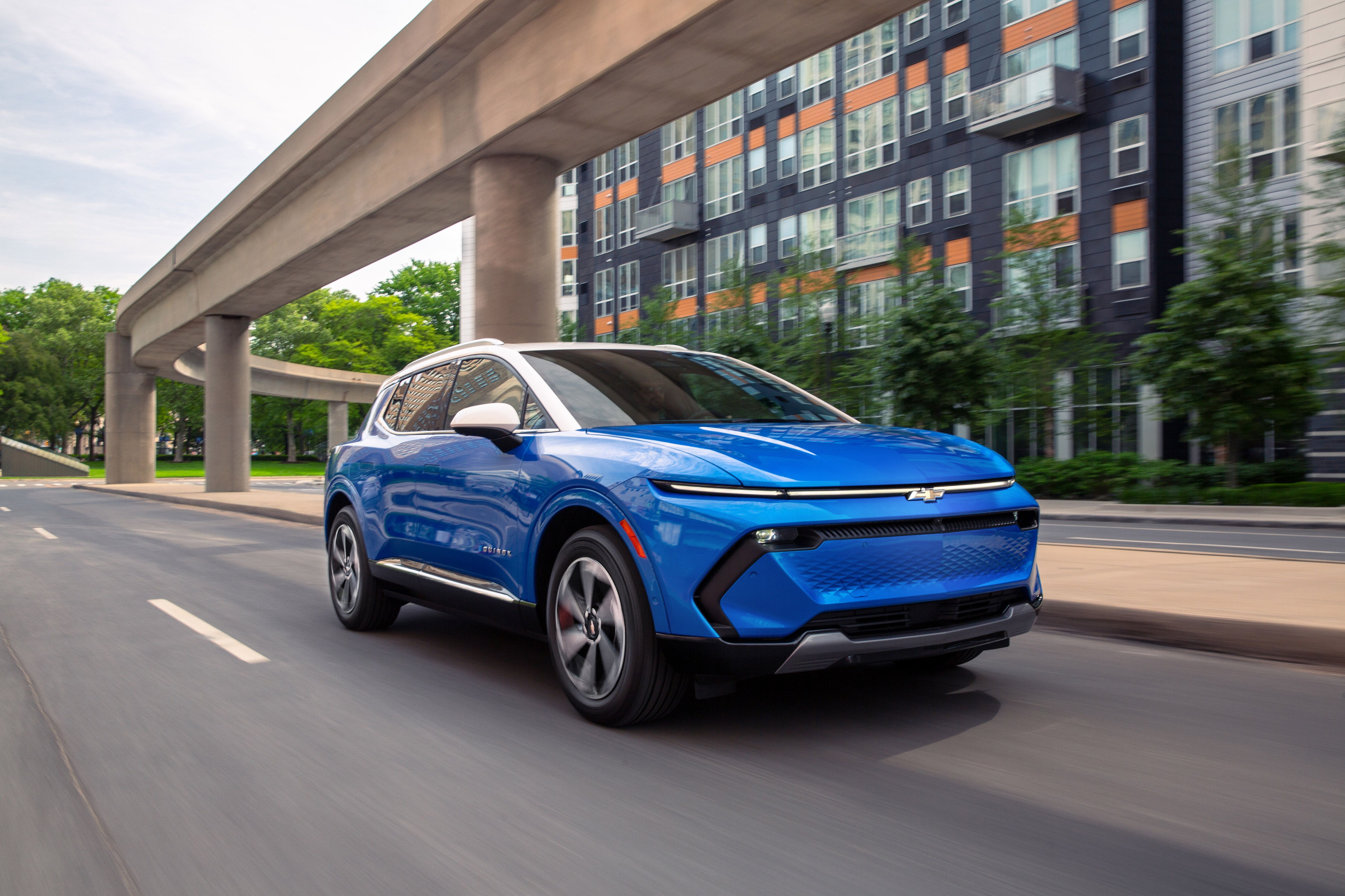 Blue Chevrolet Equinox EV driving in a city beneath a bridge.