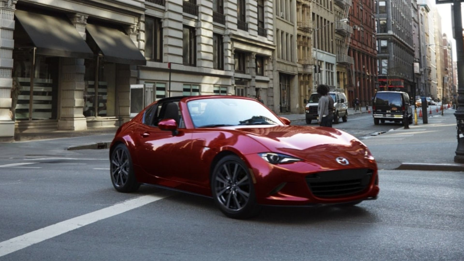 Dynamic front 3/4 shot of a red 2024 Mazda MX-5 RF driving through a city.