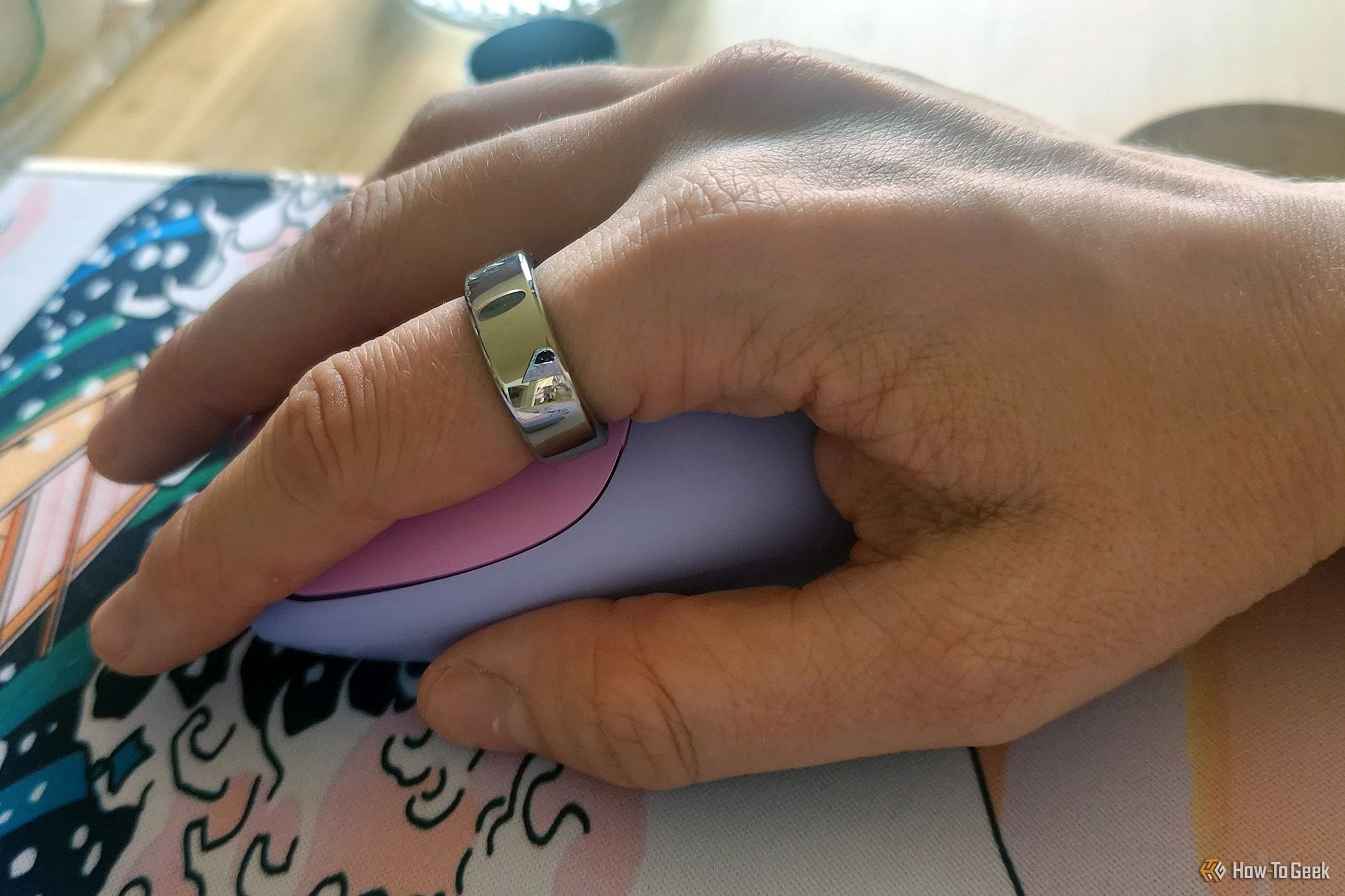 A close up of a person's hand on a computer mouse wearing the Oura Ring Generation 3 in silver.