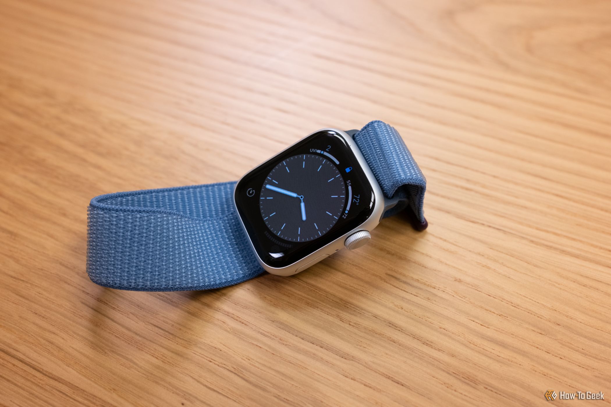 An Apple Watch Series 9 on a table top. In silver with a blue band