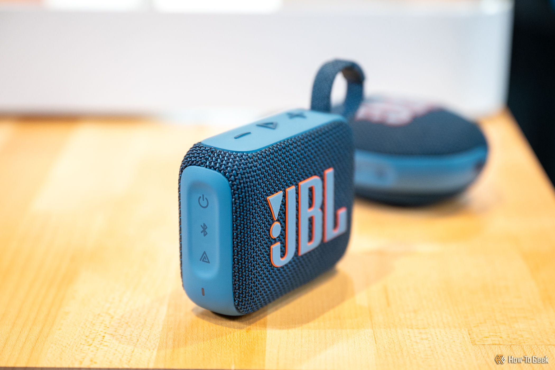 JBL Go 4 Bluetooth speaker sitting on a table in front of the JBL Clip 5.