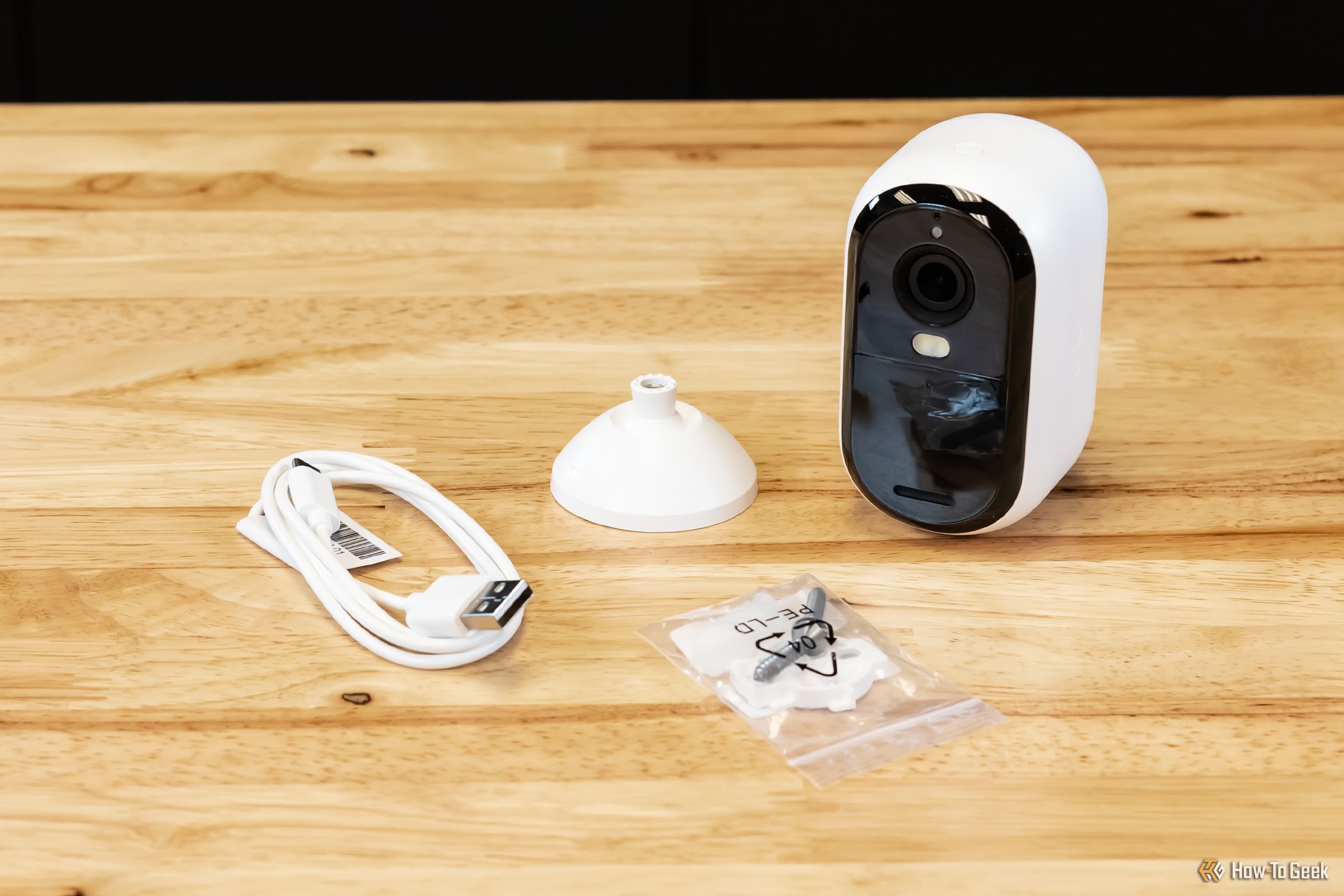 Arlo Essential 2K outdoor security camera on a wood table with included accessories.