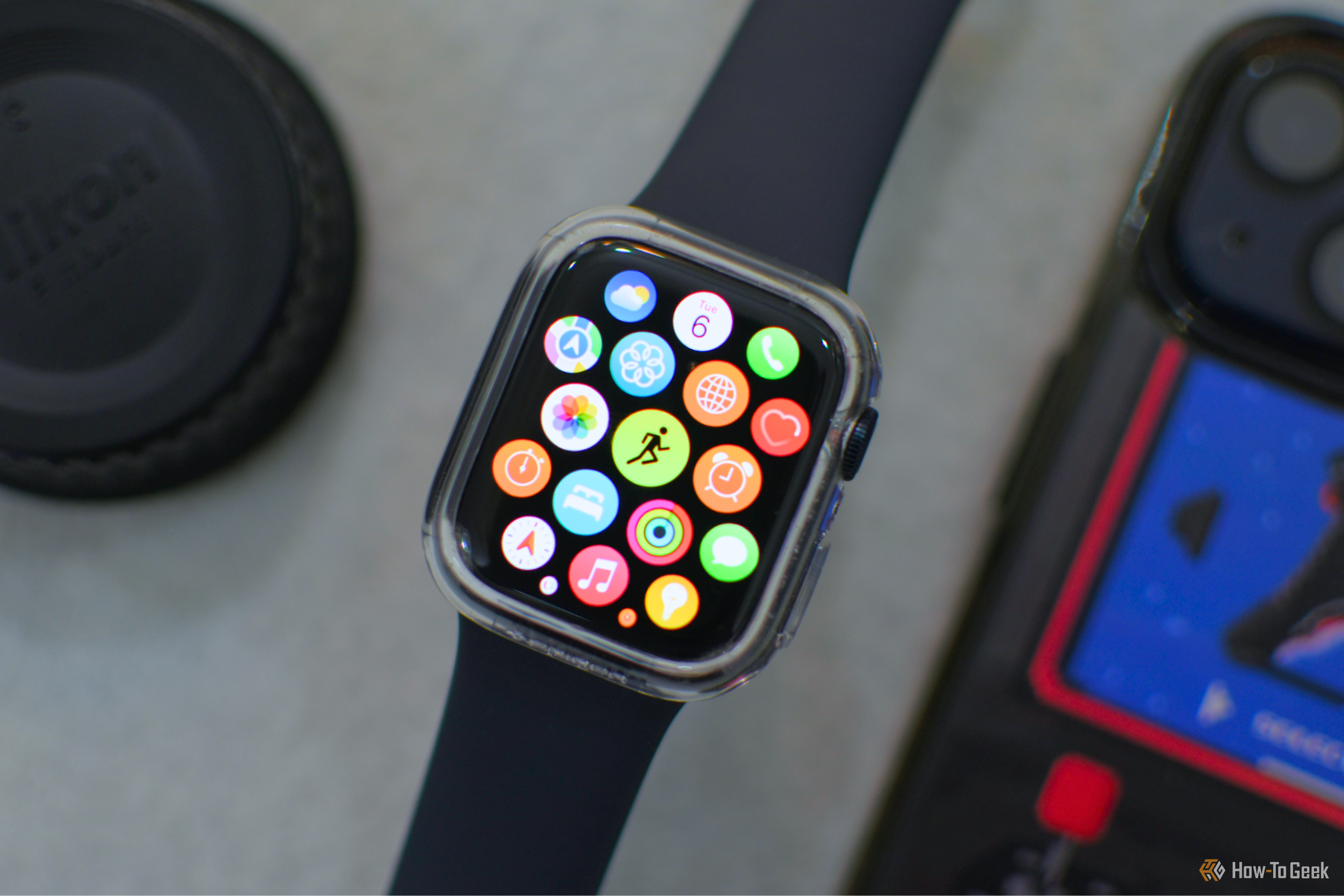 Apple Watch over a gray background with an iPhone and lens cap in the background