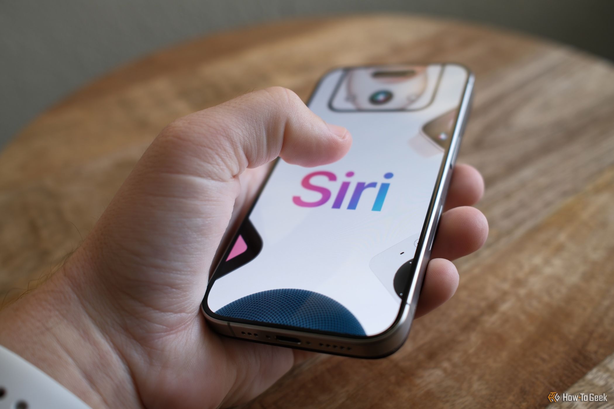 A person holding an iPhone with the word Siri on screen.