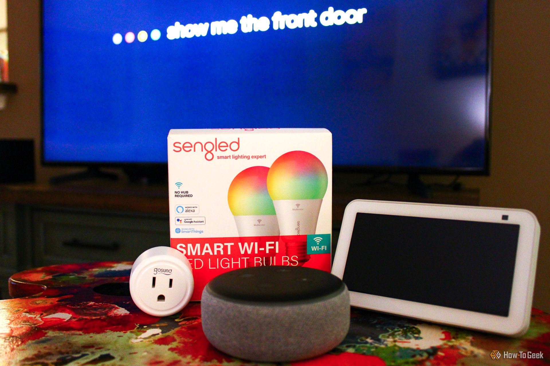 A smart TV flanked by an Echo Dot and Echo Show, a smart plug, and smart light bulbs.