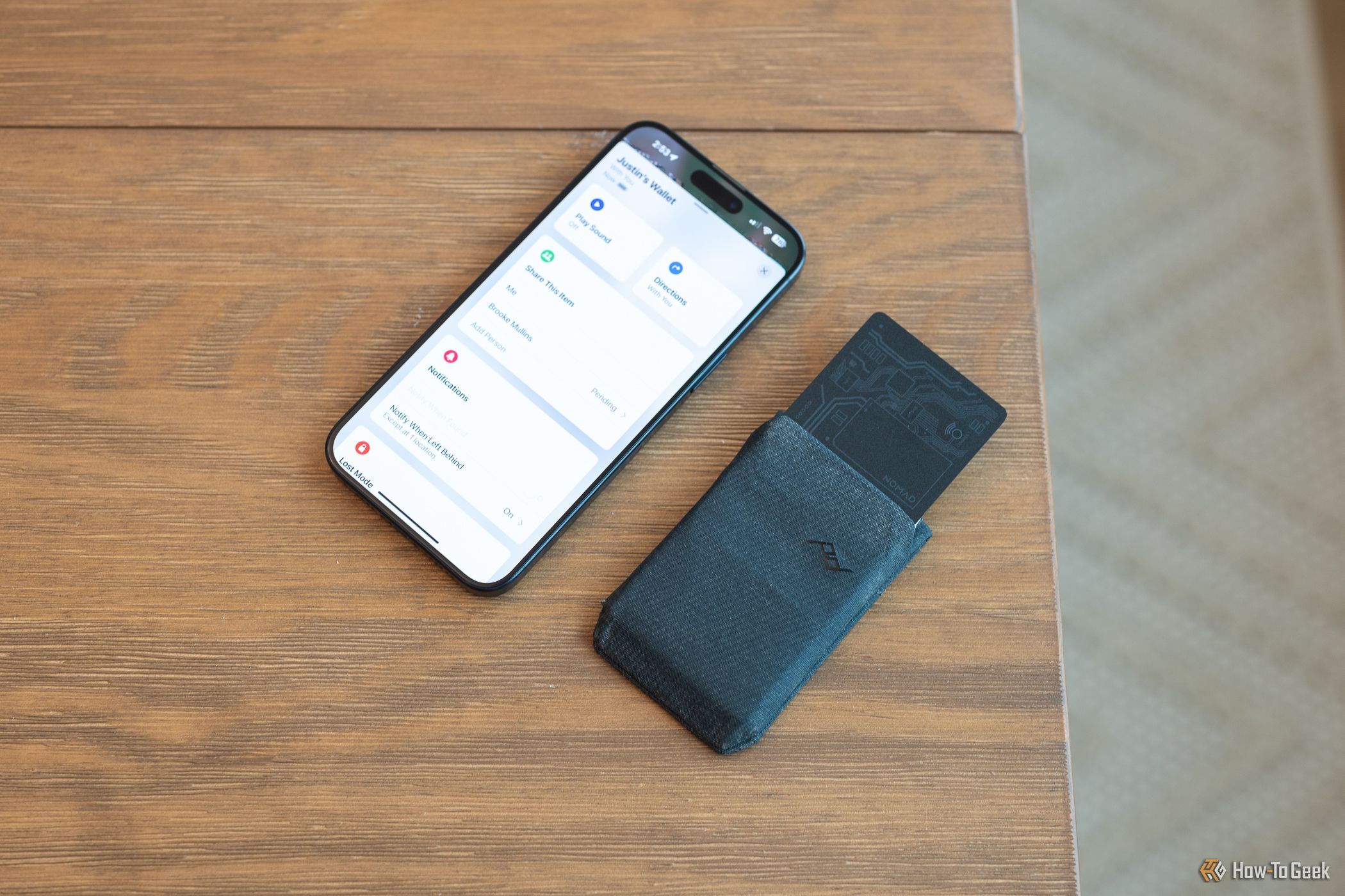 Nomad Tracking Card sticking out of a wallet next to an iPhone showing the Find My app