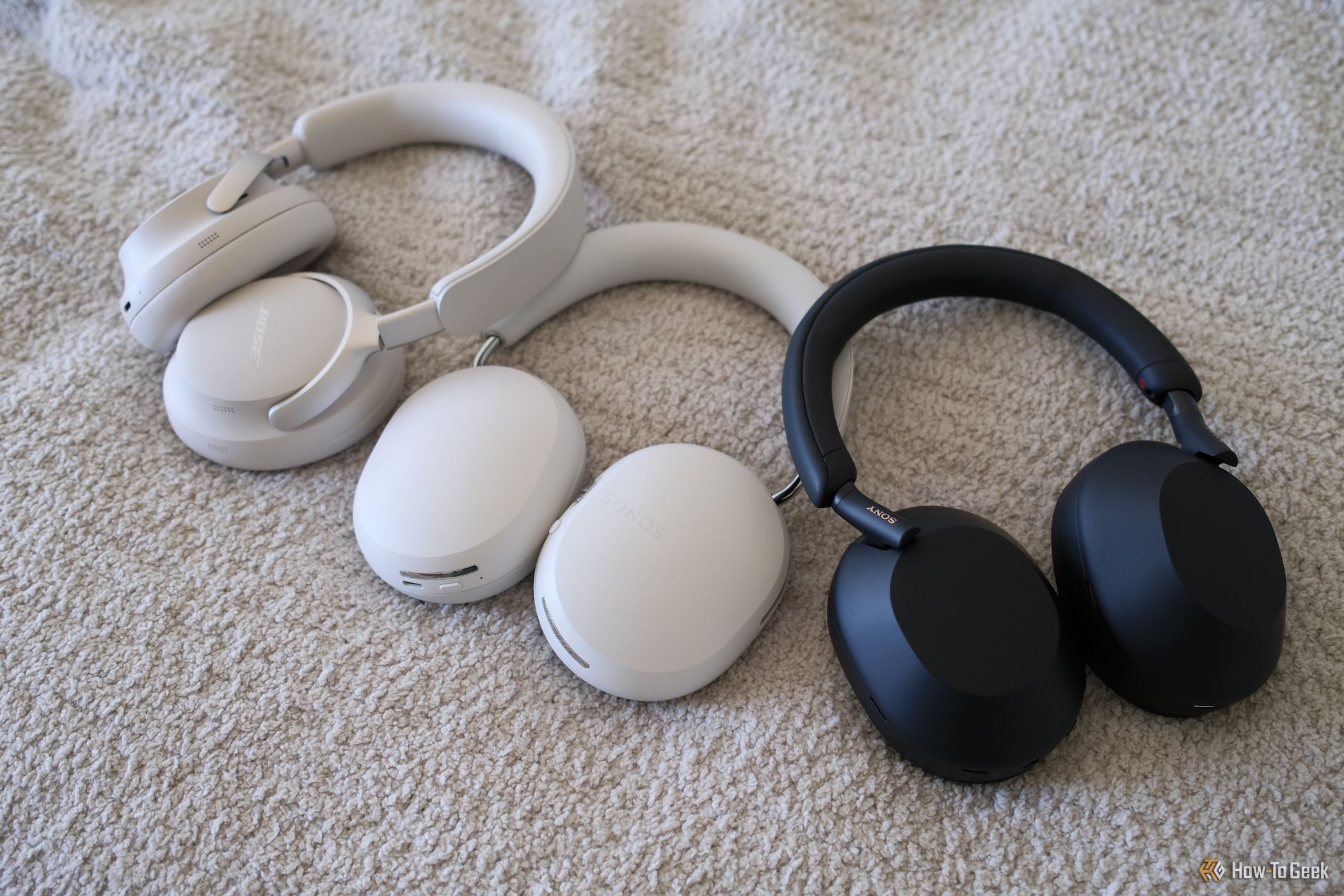 The Sonos Ace lying next to Bose and Sony headphones on a white surface.