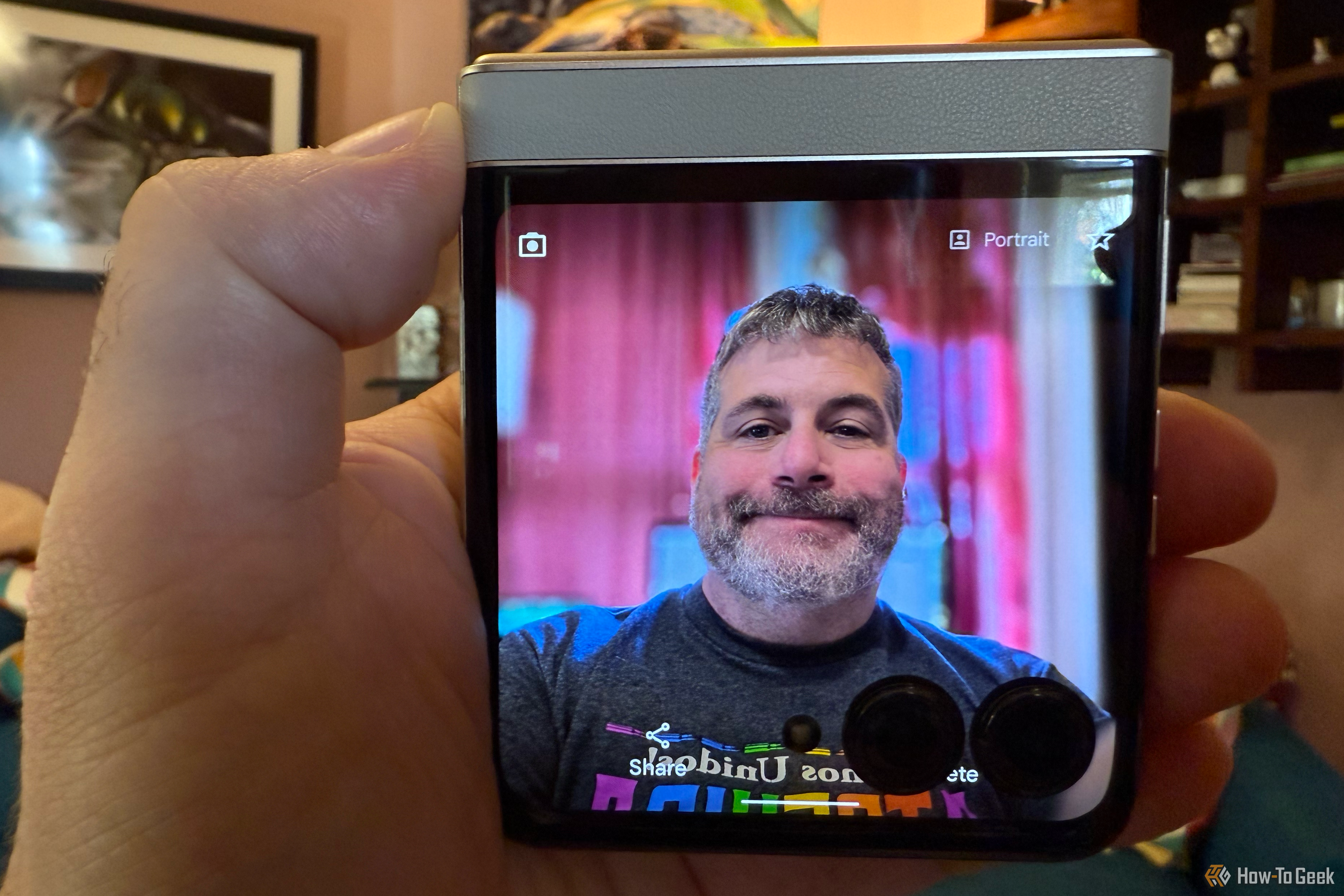 The Motorola Razr facing the camera, showing the selfie portrait mode. A hand holds the phone, and a man is seen on the screen posing for a photo.