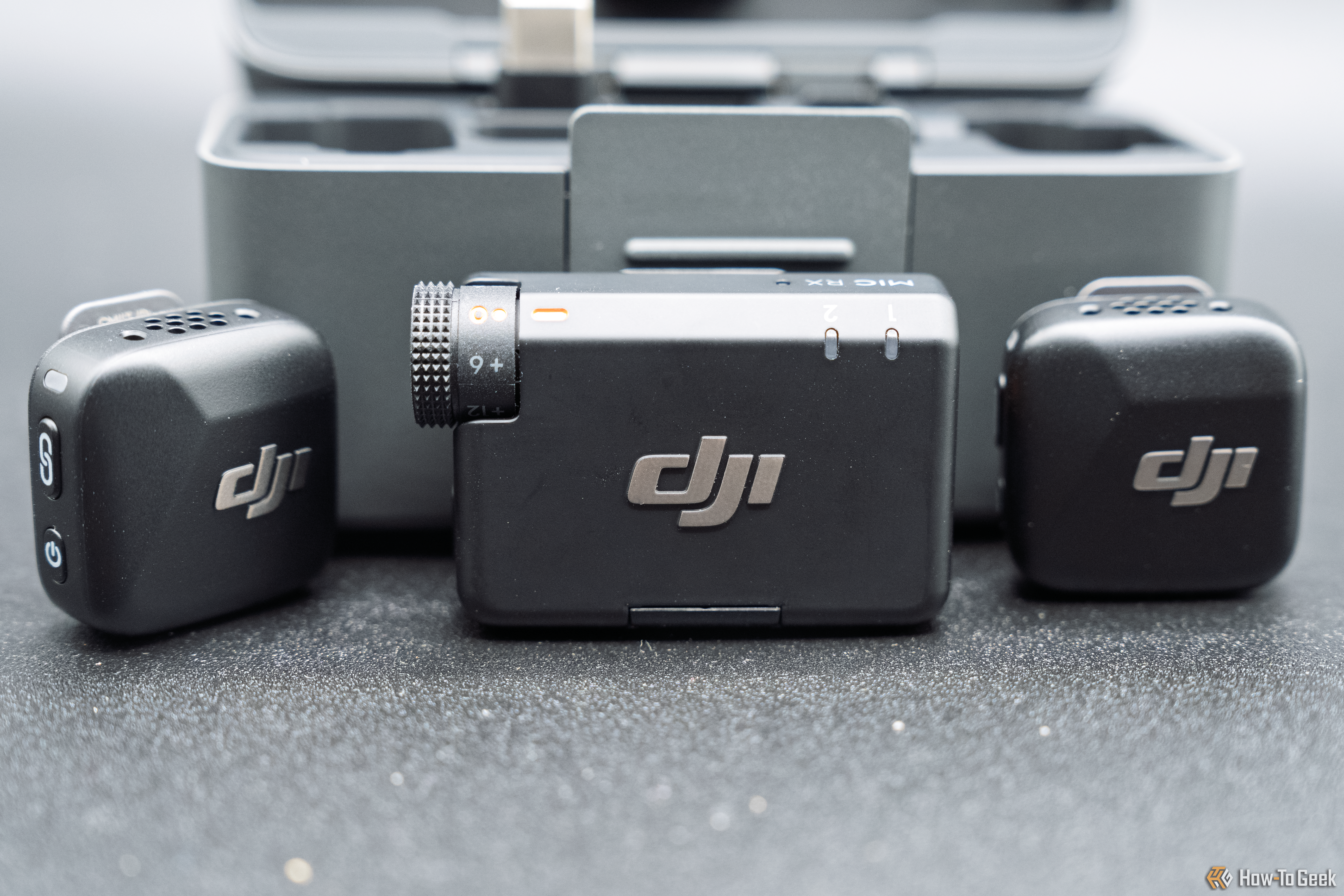 The microphones and receiver in front of the charging storage case, on a gray background.