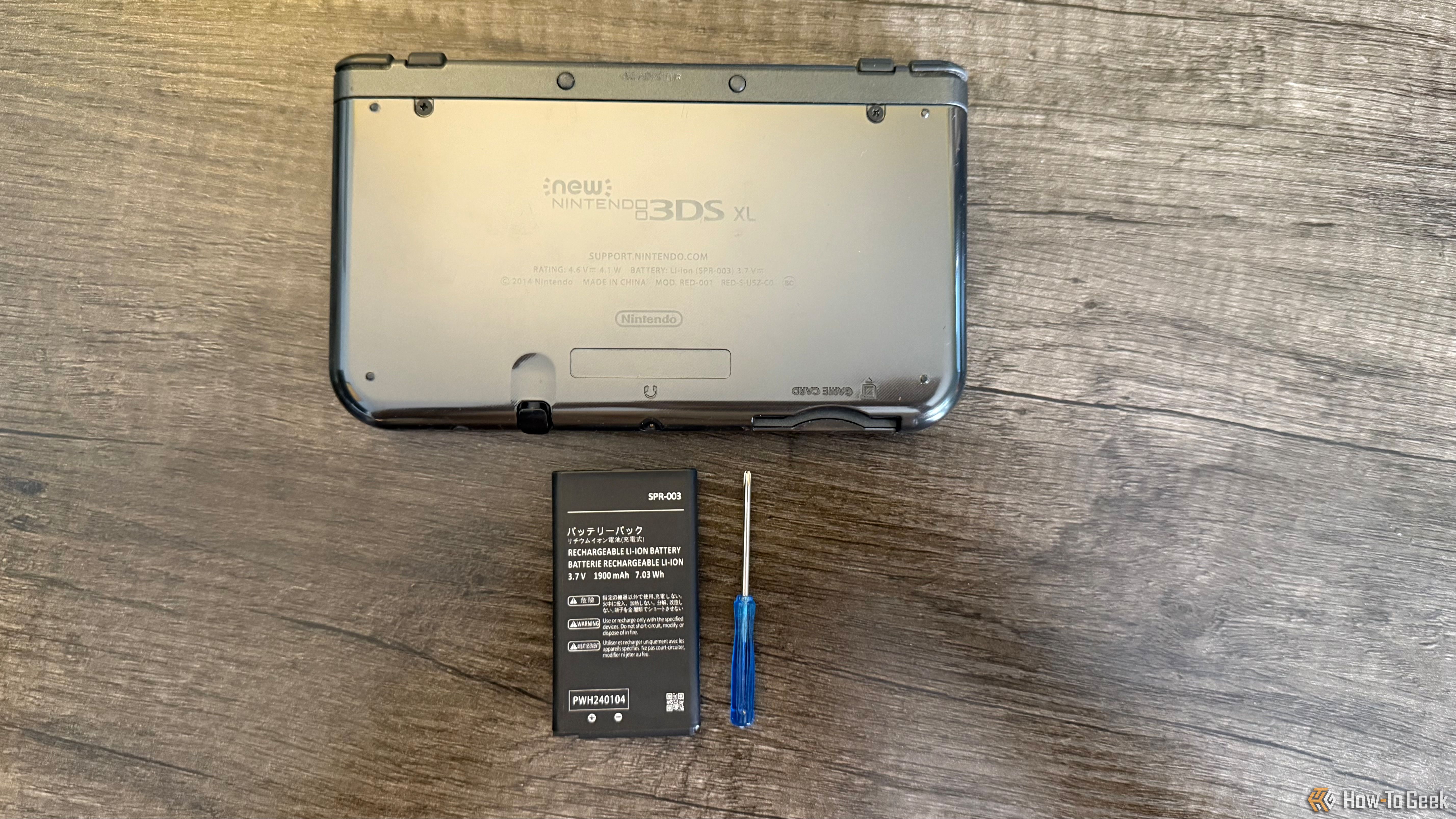 The back of a New Nintendo 3DS XL with a replacement battery and screwdriver.