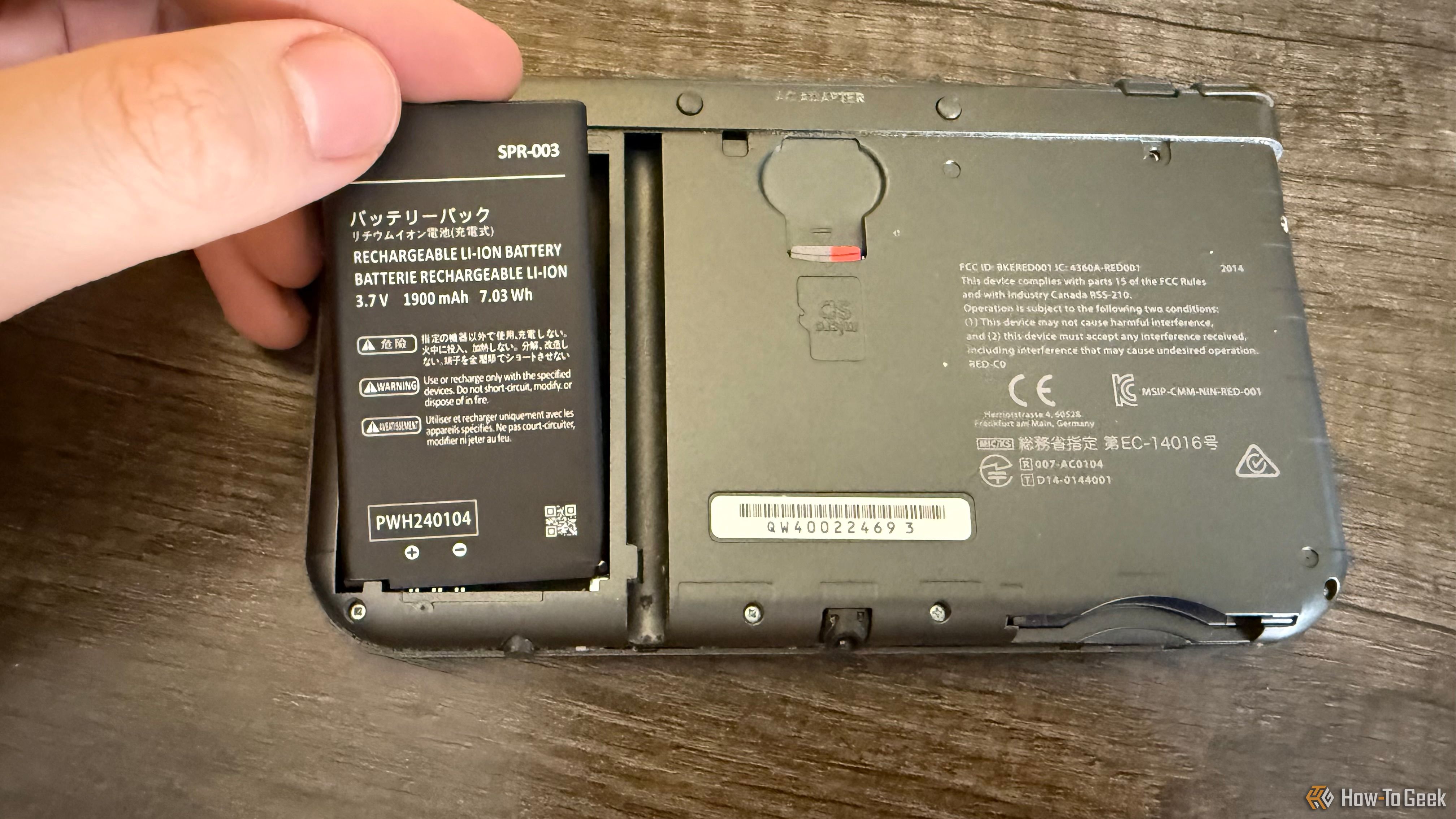 A hand placing a battery pack into a New Nintendo 3DS XL.