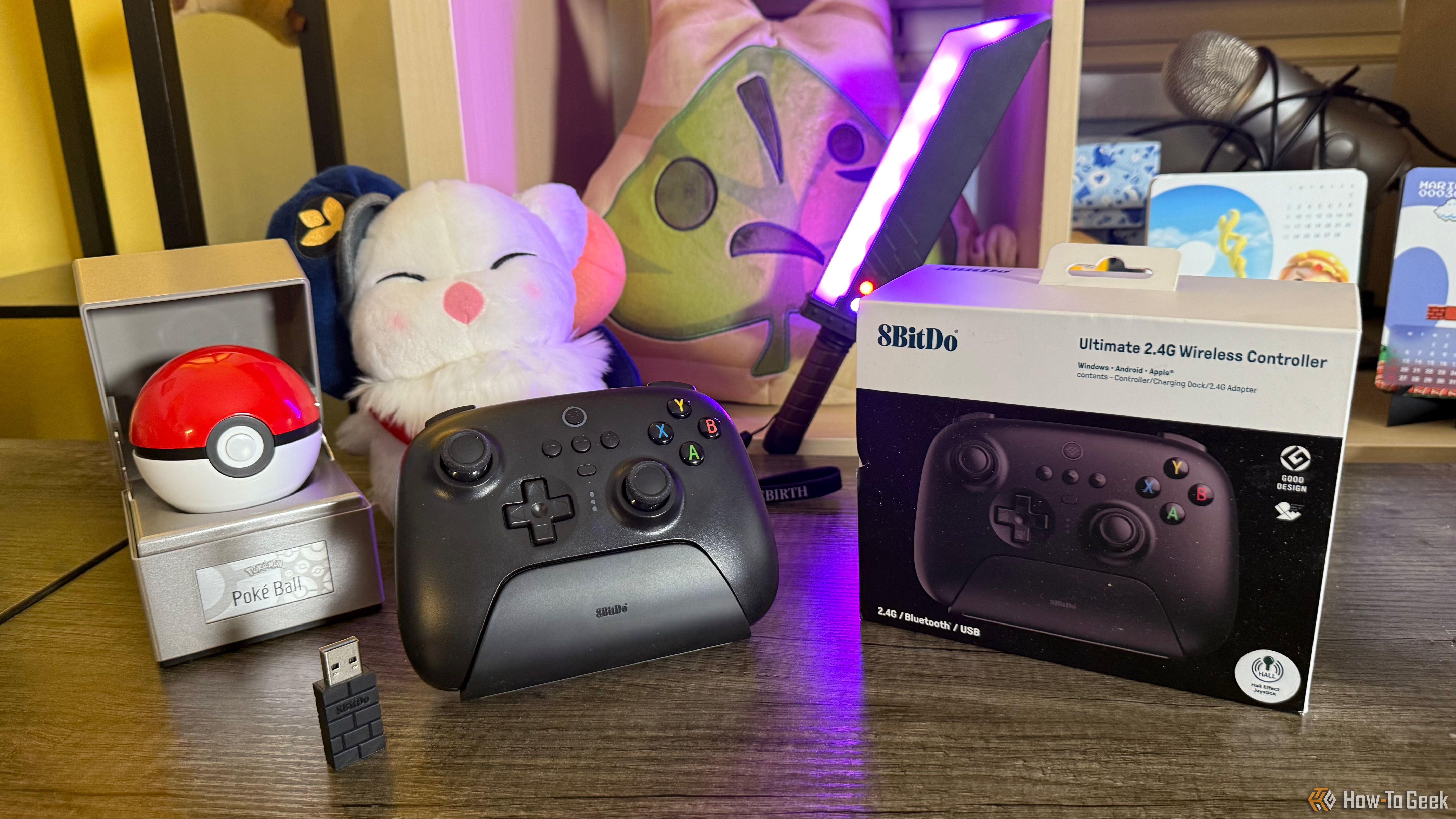 8BitDo Ultimate 2.4G Controller on a table with its 2.4 GHz receiver, dock, packaging, and gaming merchandise.