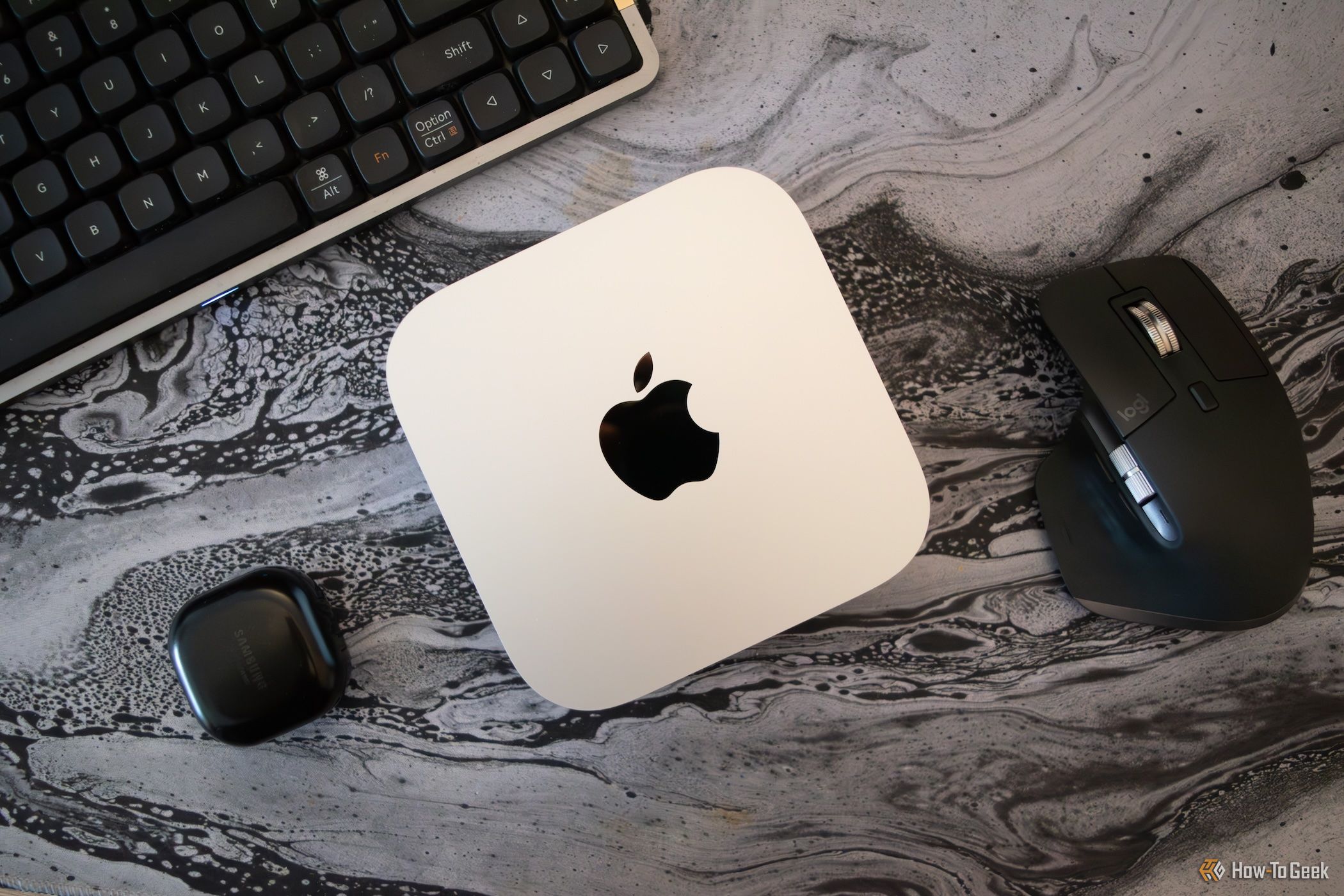 An M4 Mac Mini sitting on a desk encircled by various PC peripherals. 