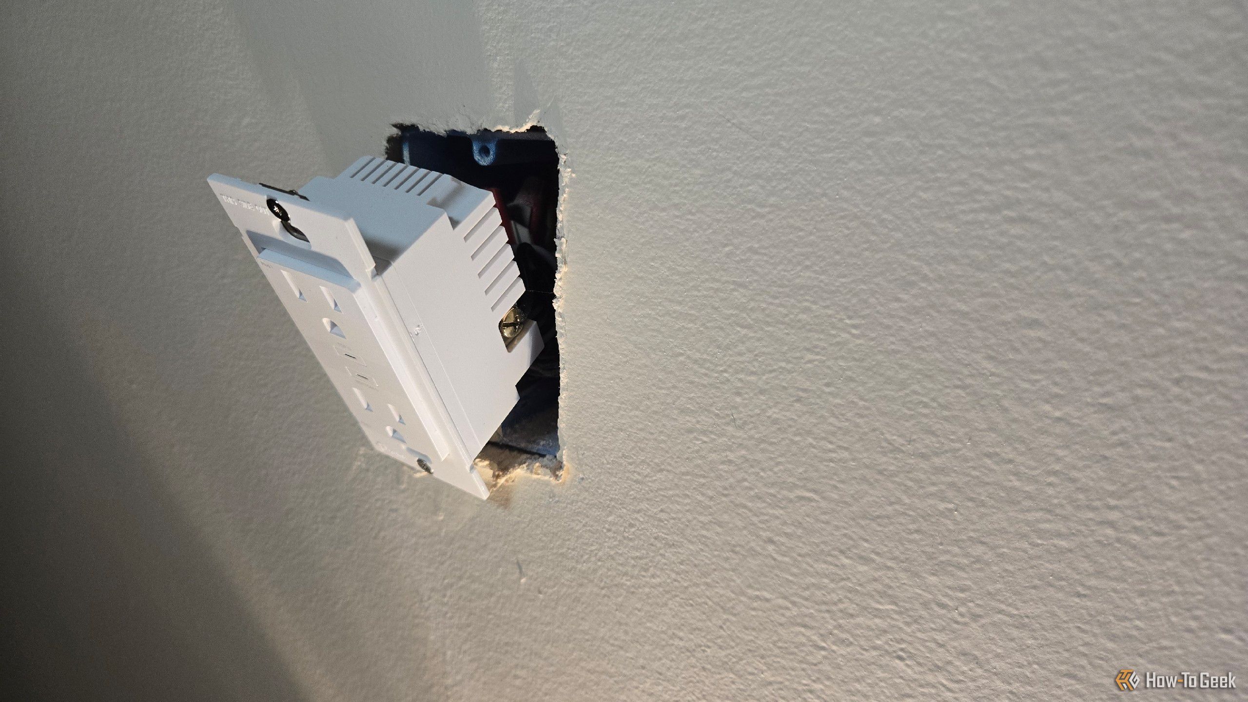 A TP-Link Tapo P210M smart outlet hanging partly out of a wall.