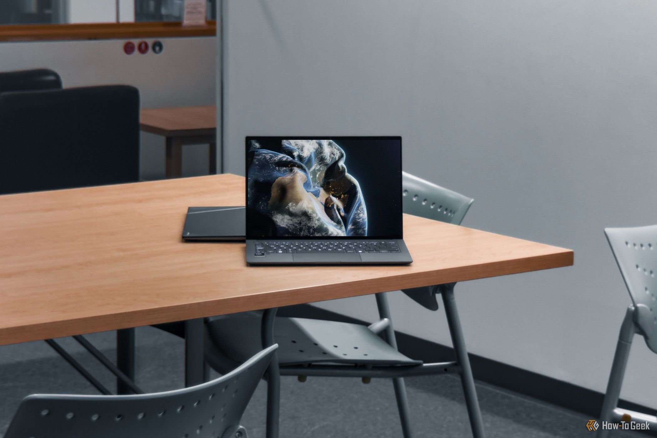 ASUS Zenbook S 14 with screen on, on wooden table (wide shot).