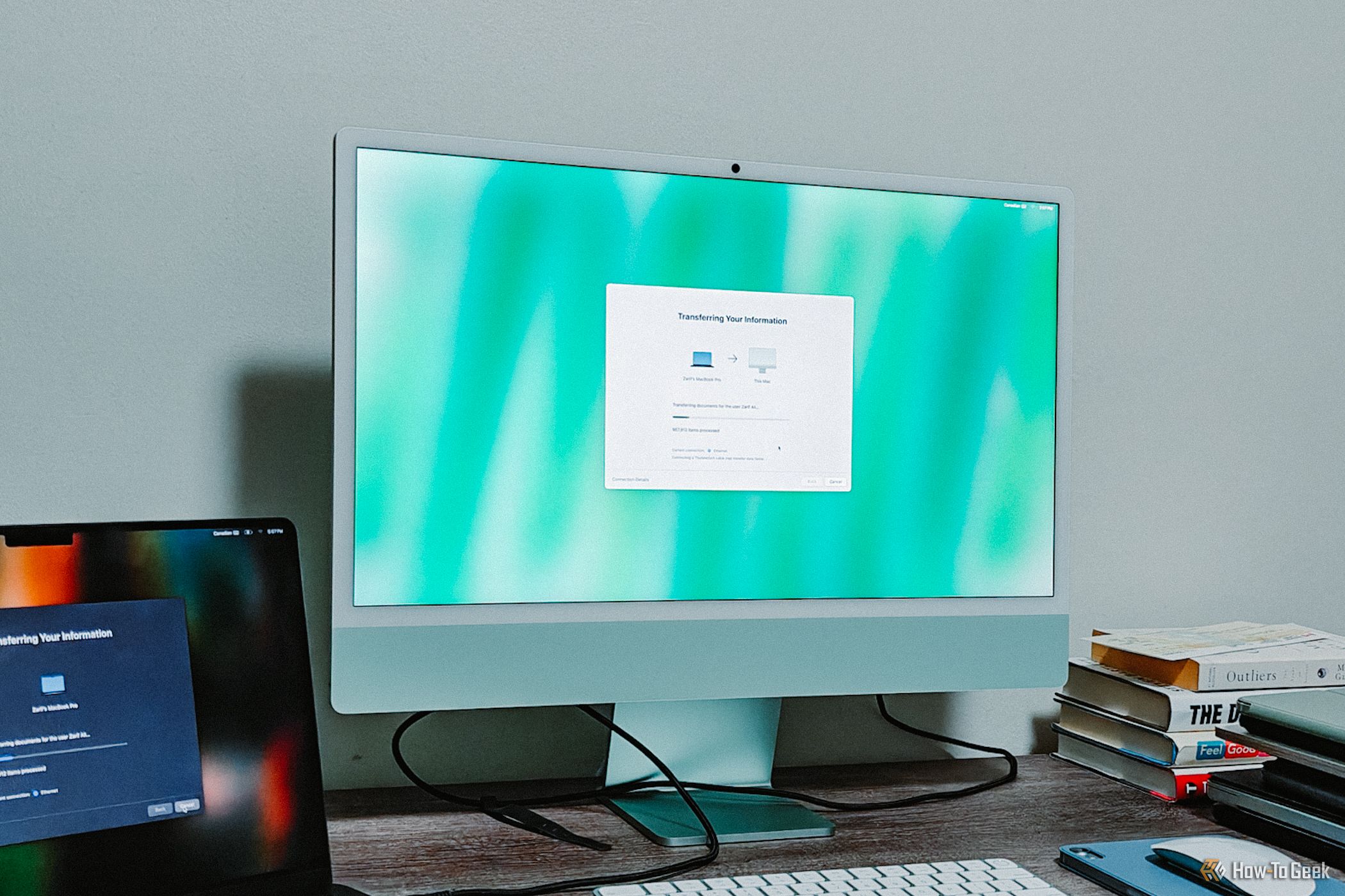 Green M4 iMac screen with MacBook Pro by its side.