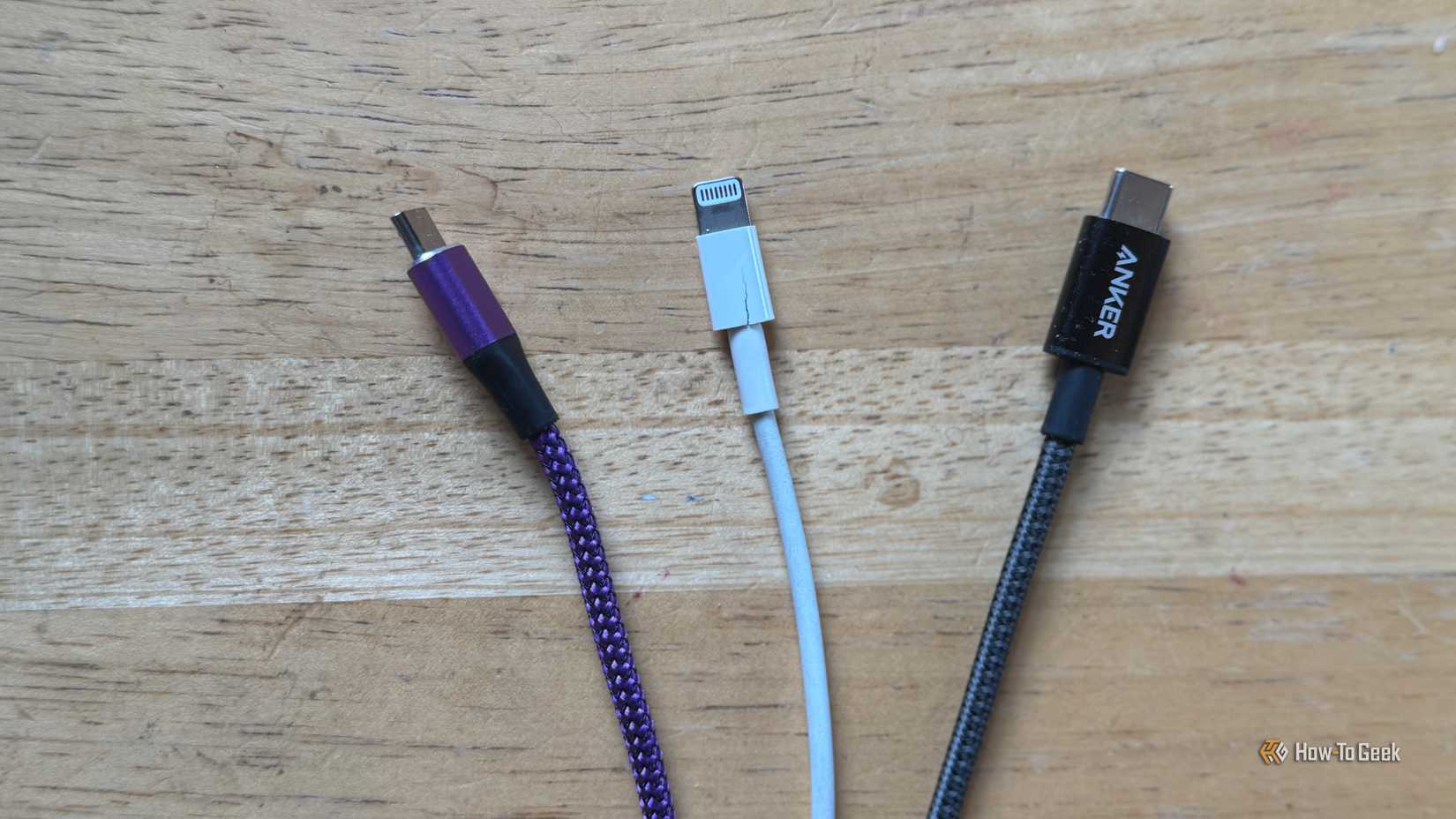A purple micro-USB cable, a white Lightning cable, and a gray USB-C cable on a table