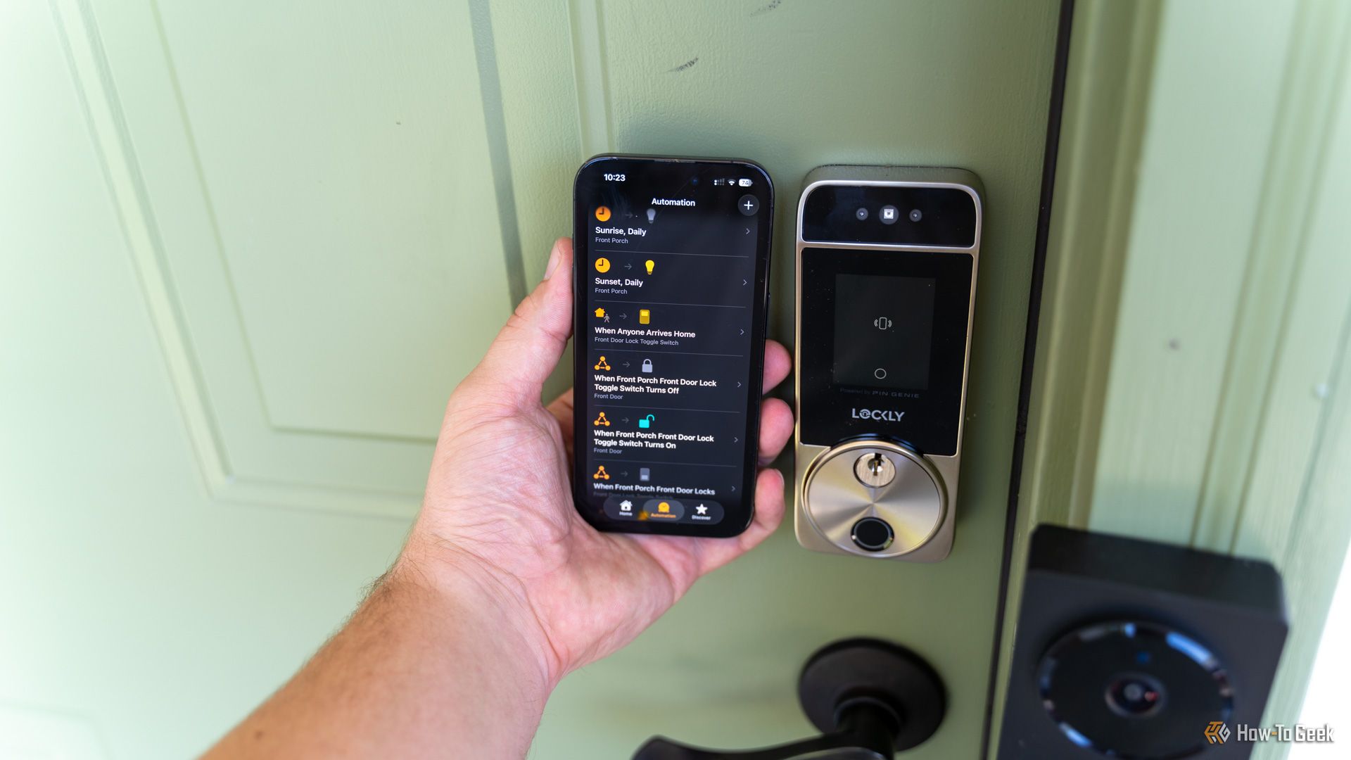 An iPhone with the Apple Home app opened showing automations being held next to a Lockly Visage smart lock.