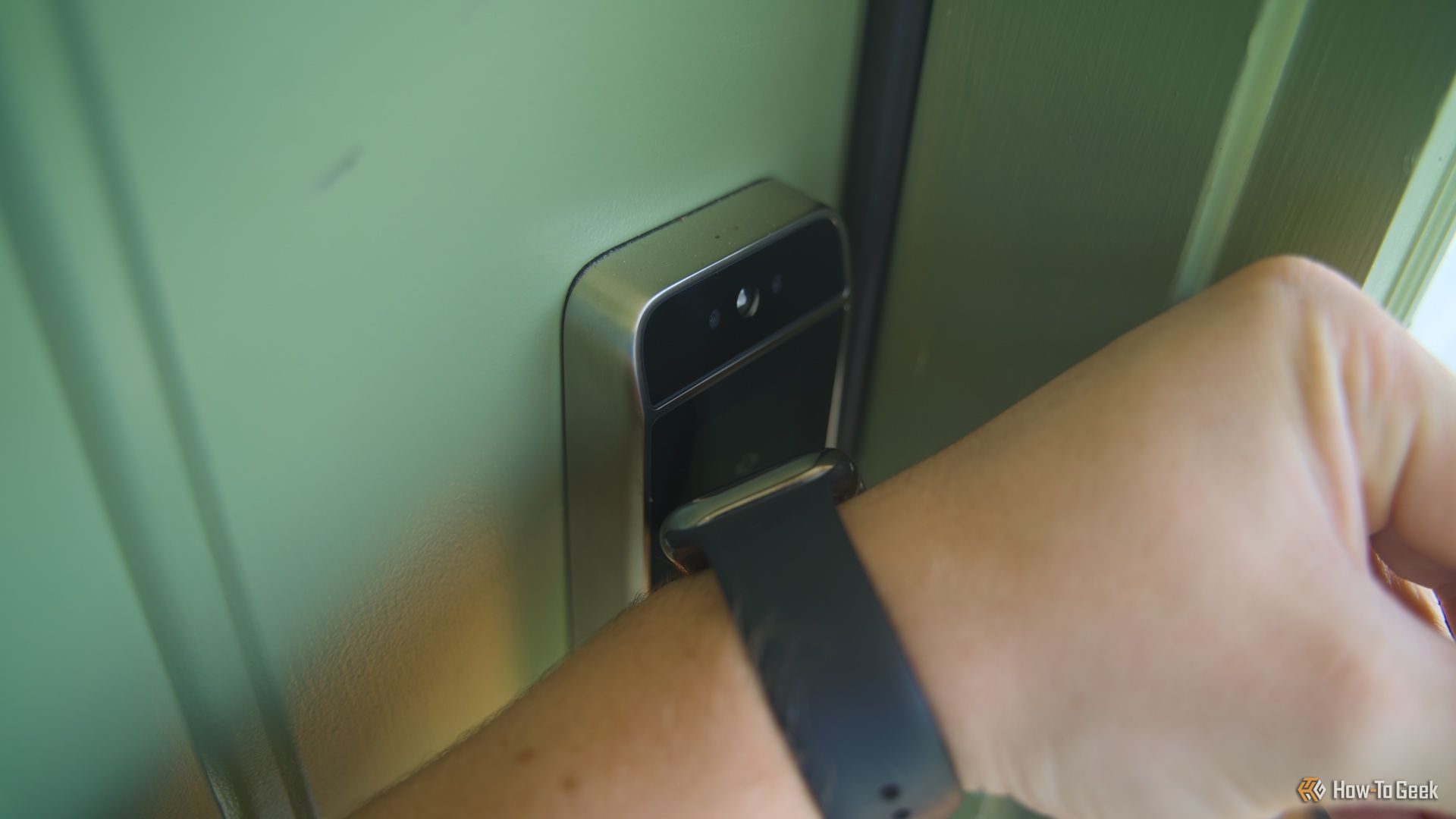 An Apple Watch being held to the Lockly Visage smart lock to use Apple Home Key to unlock the front door.
