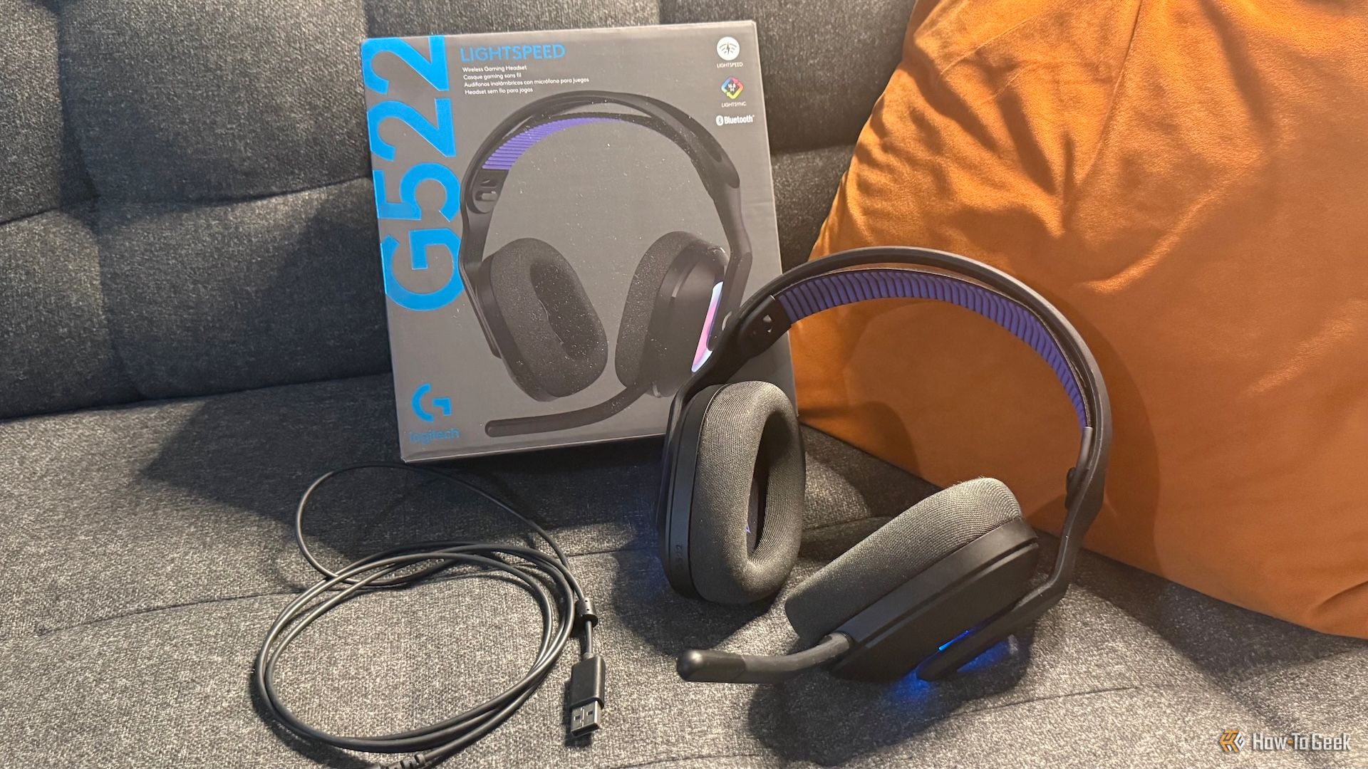 The Logitech G522 Lightspeed gaming headset, its USB cord, and its box on a couch.