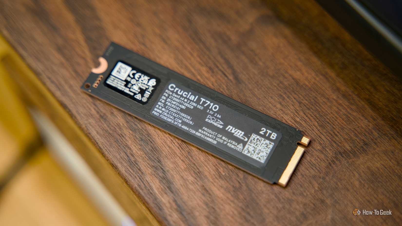 The back of the Crucial T710 NVMe SSD sitting on a walnut shelf.